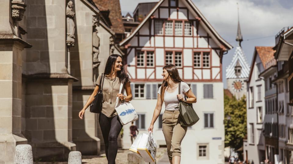 Zwei Damen laufen mit vollen Shoppingtaschen durch die Zuger Altstadt.