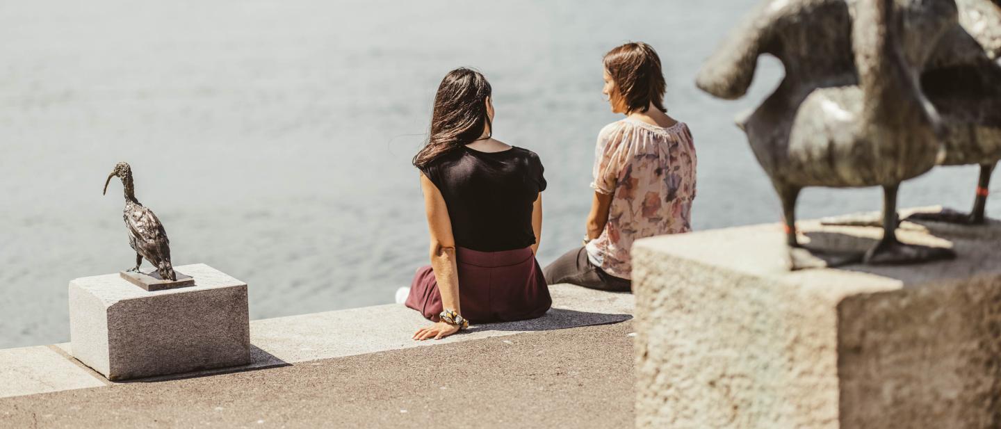 Zwei Frauen sitzen am Ufer des Zugersee vor Kunstwerken im öffentlichen Raum