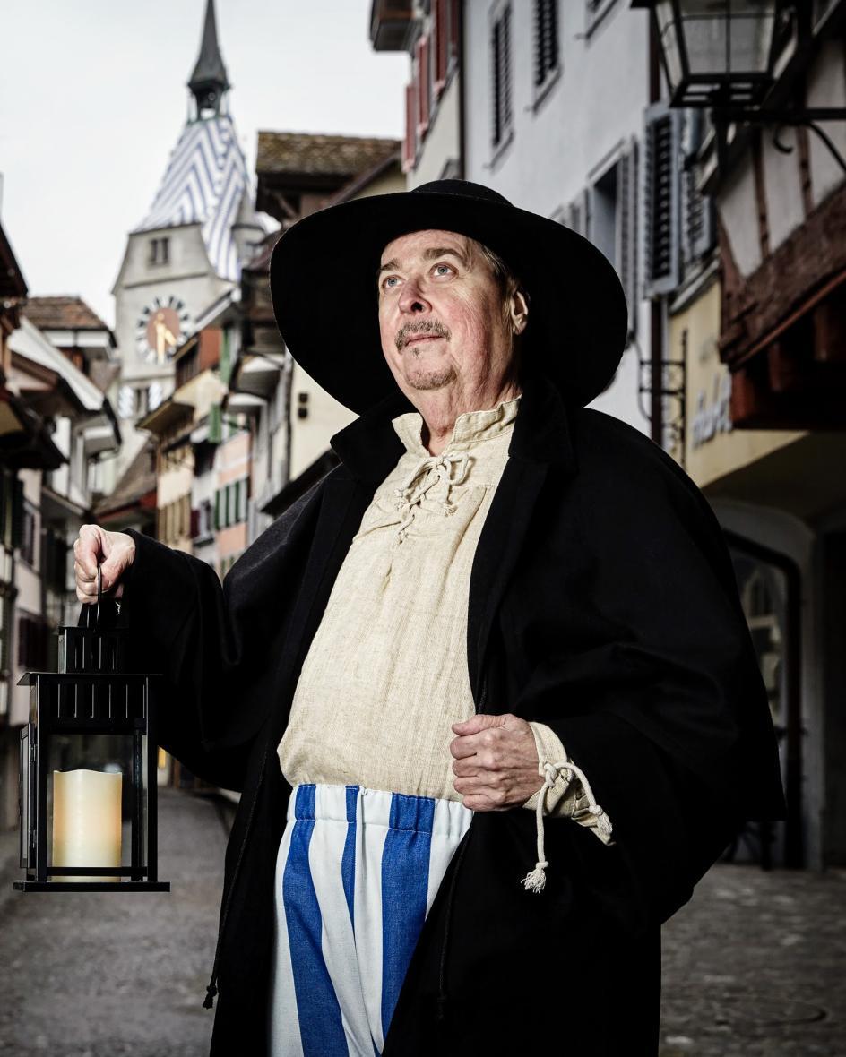 Stadtführer steht in historischen Kleidern mit einer Laterne in der Hand in der Zuger Altstadt.
