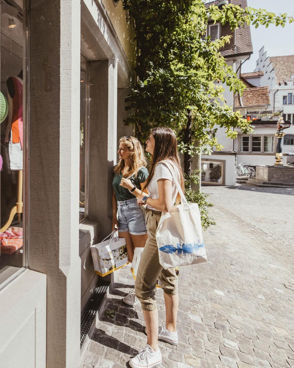 Zwei Damen bestaunen ein Kleiderladen Schaufenster in der Zuger Altstadt.