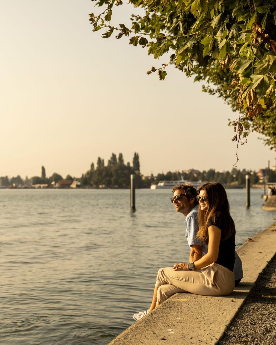 Eine Frau und ein Mann sitzen am Ufer des Zugersees und schauen in den Sonnenuntergang.
