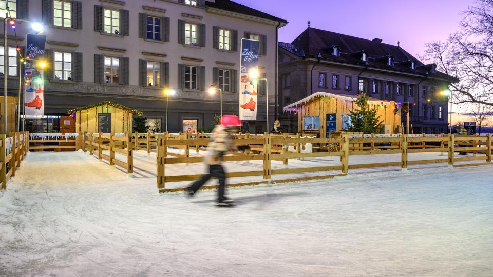 Ein Kind ist vor dem alten Postgebäude in Zug am Eislaufen.