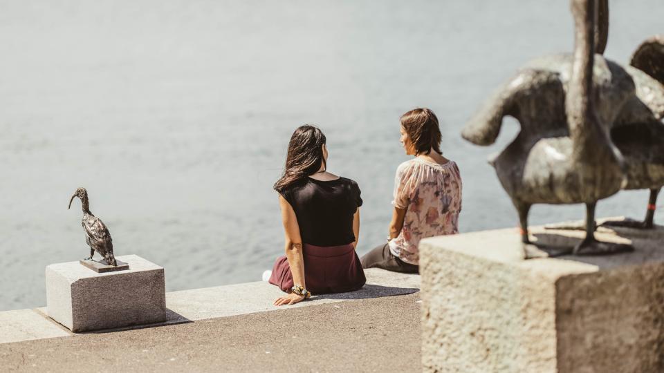 Zwei Frauen sitzen am Ufer des Zugersee vor Kunstwerken im öffentlichen Raum