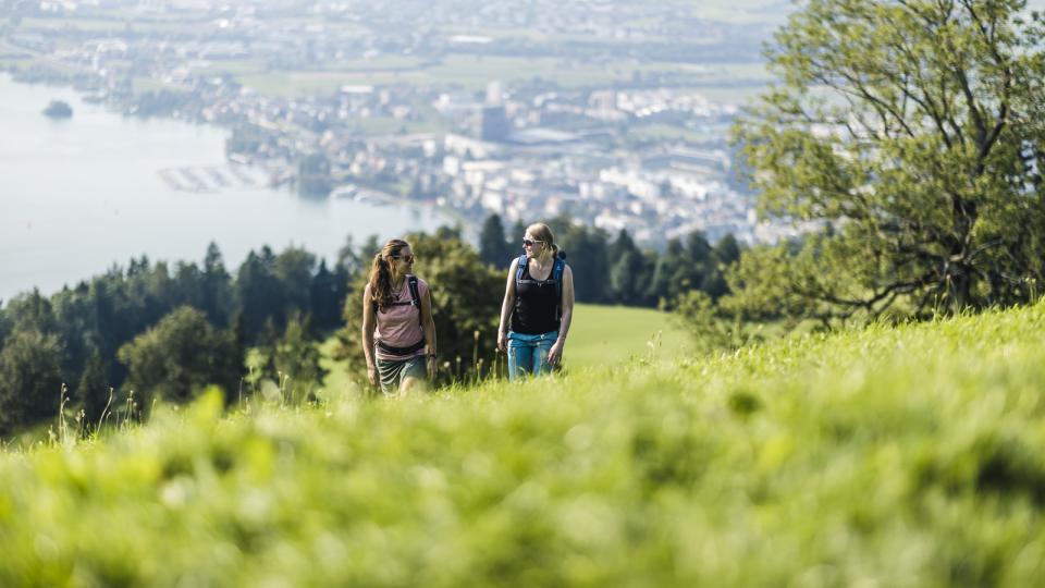 Zwei Frauen wandern auf den Zugerberg. Im Hintergrund ist der See und die Stadt Zug zu sehen.