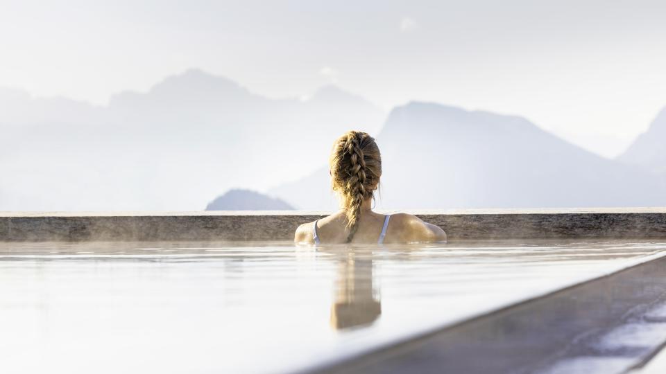 Eine Dame badet im Aussenbecken des Mineralbads und Blickt auf das Bergpanorama.