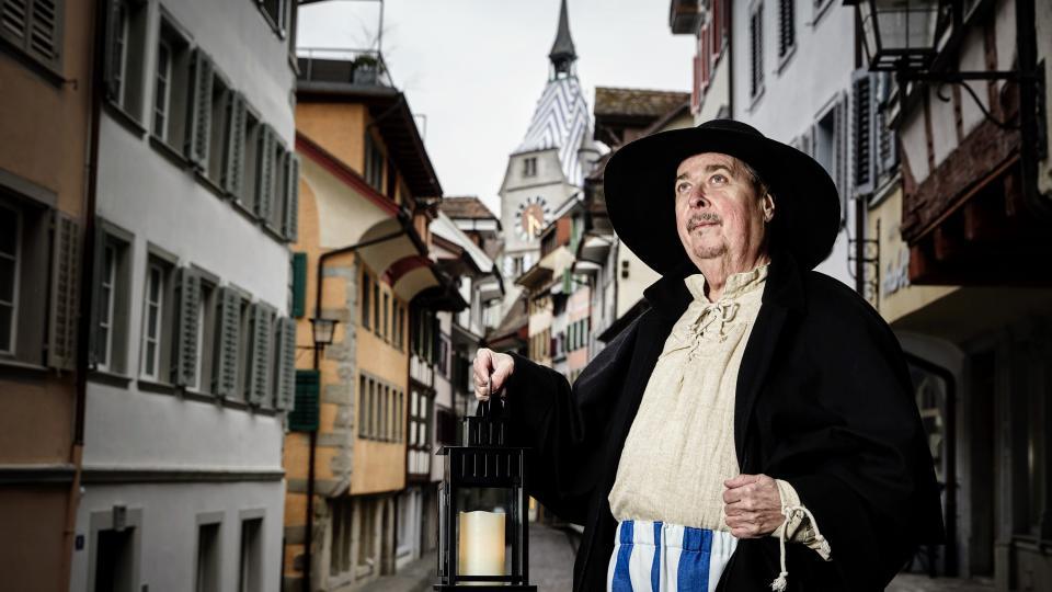 Stadtführer steht in historischen Kleidern mit einer Laterne in der Hand in der Zuger Altstadt.