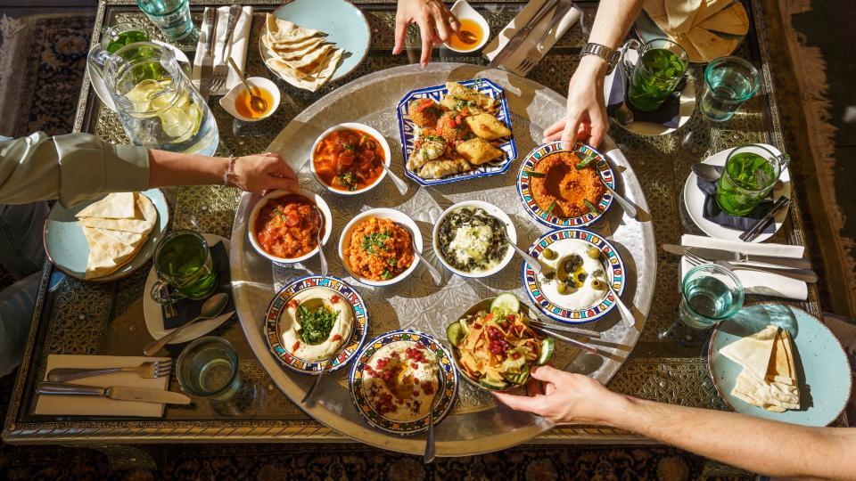 Ein Tisch ist bedeckt mit Mezze Gerichen und vier Hände greifen nach den Speisen.