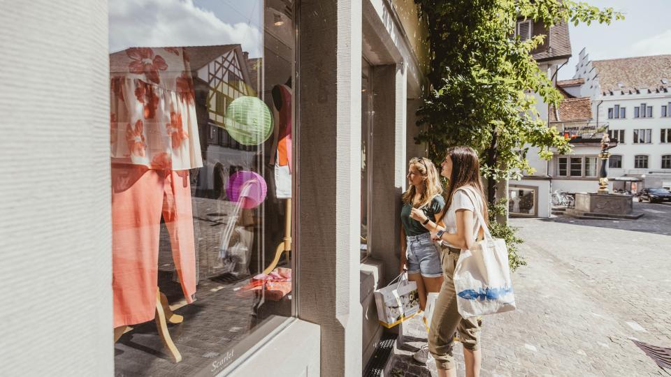 Zwei Damen bestaunen ein Kleiderladen Schaufenster in der Zuger Altstadt.