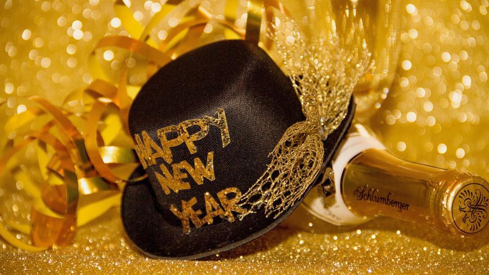 Ein schwarzer Hut mit der Schriftzug Happy new year liegt auf einer Sektflasche.