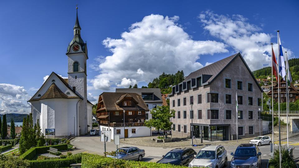 Die Kirche Walchwil steht vor einem historischen Holzgebäude.