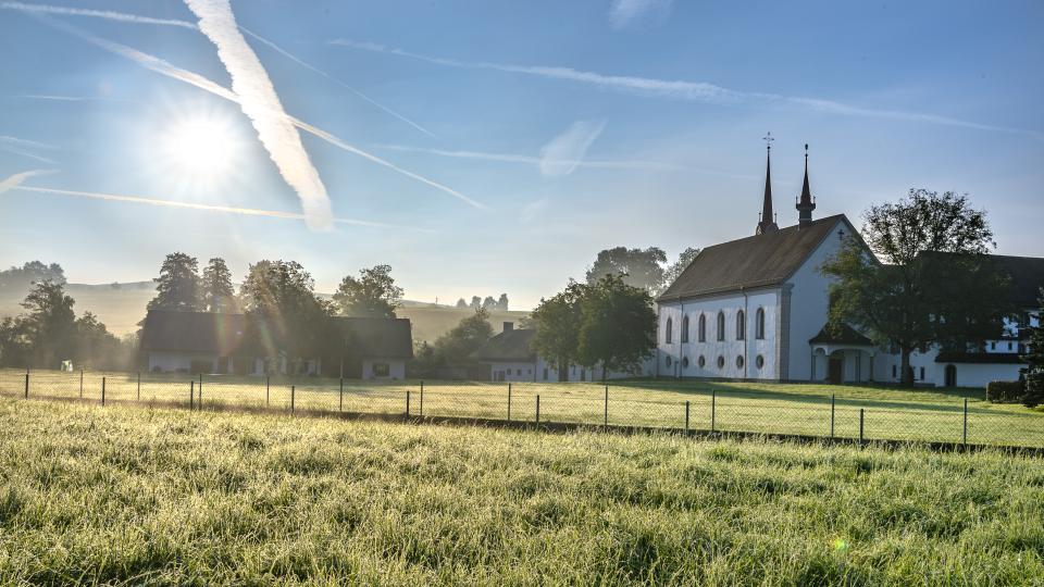 Das Kloster Frauental steht auf einer grünen Wiese. Am blauen Himmel sind Kondensstreifen zu sehen.