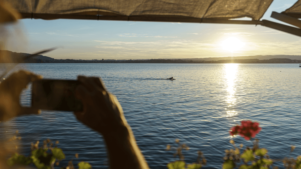 Ein Person fotografiert mit einem Smartphone den Sonnenuntergang über dem Zugersee.