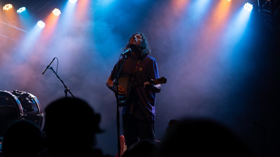Ein Musiker mit Gitarre steht auf der Bühne und schaut nach oben.