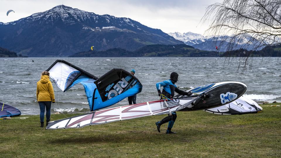 Ein Wind- und Kitesurfer machen sich auf der grünen Wiese am Ufer des Zugersees parat.