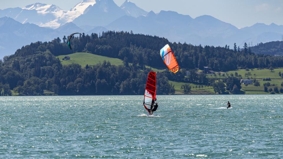 Ein Wind- und Kitesurfer sind vor den schneebedeckten Berner Alpen auf dem Wasser.