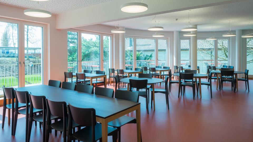 Speisesaal mit rotem Boden, braunen Holztischen und einer grossen Fensterfront der Jugendherberge Zug.