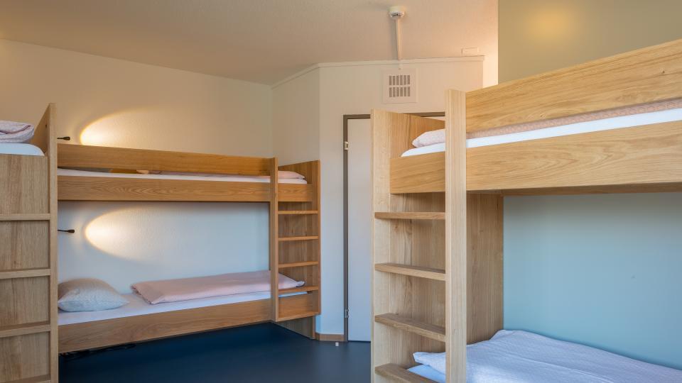 Zwei Doppelstockbetten mit weisser Bettwäsche stehen im Zimmer mit einem dunkelblauen Boden.