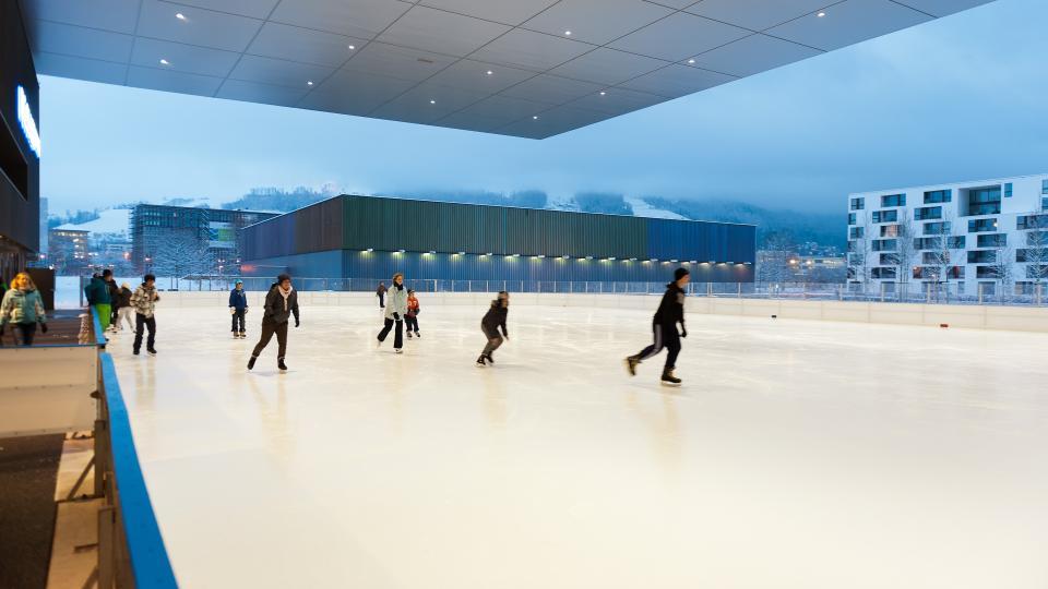 Schlittschuhlaufende auf dem Ausseneisfeld der Bossard Arena mit Blick auf den verschneiten Zugerberg.