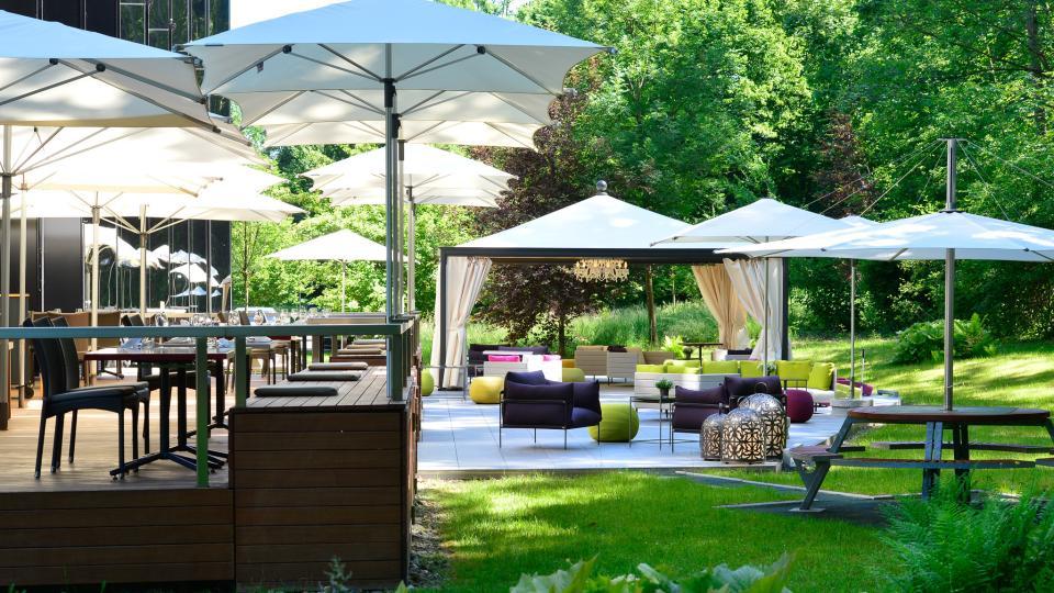 Über der Terrasse des Restaurants City Garden sind helle Sonnenschirme aufgespannt. Richtung Wald liegt die Lounge des Secret Garden.