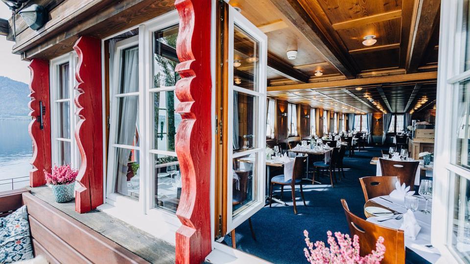 Blick durchs Fenster ins Restaurant mit gedeckten Holztischen und blauem Boden.