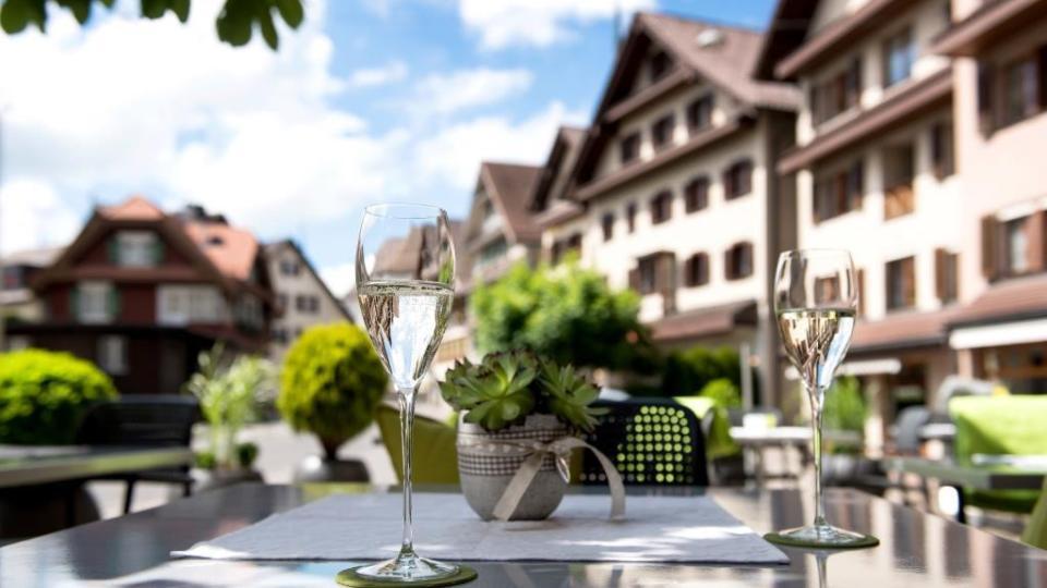 Auf dem Gartentisch stehen zwei Weissweingläser und im Hintergrund ist die Fassade des Hotels erkennbar.