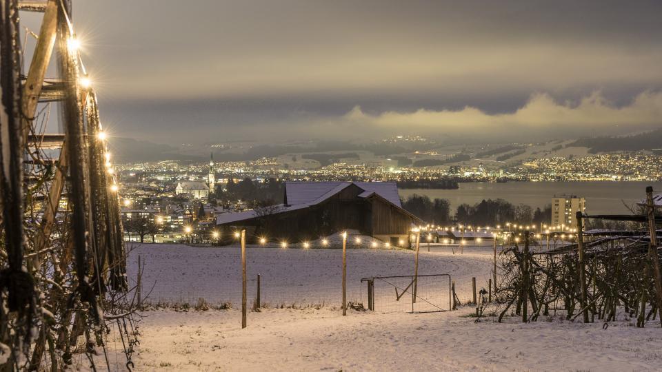 Lichterkette in der verschneiten Landschaft mit Blick auf den Zugersee auf dem Lichterwerg Hühnenberg