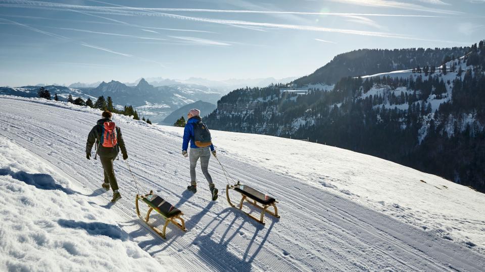 Zwei Personen ziehen den Schlitten auf der frisch präparierten Strecke den verschneiten Berg hoch mit Blick auf den Mythen.