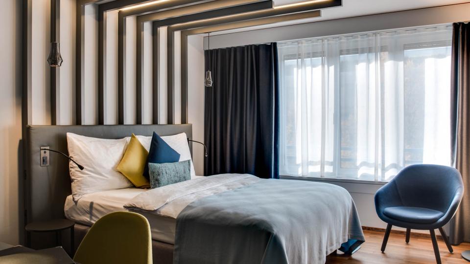 Farbig bezogenes Bett steht auf einem hellen Holzboden des Parkhotels Zug.