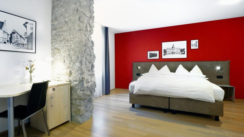 Premium Zimmer mit Doppelbett auf Holzboden und vor roter Wand.