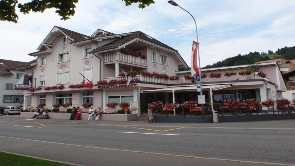 Aussenansicht des Hotels mit Busparkplatz im Vordergrund und Geranien auf den Balkonen.