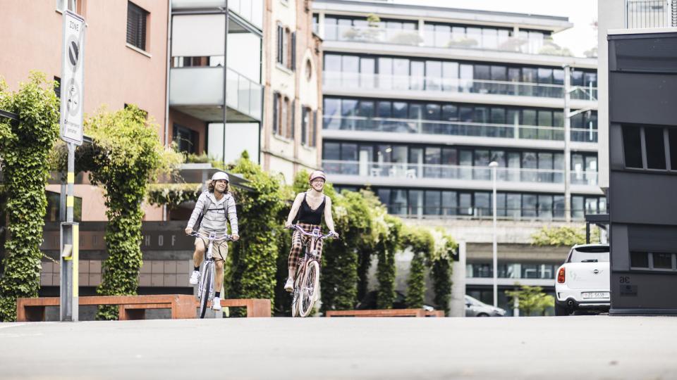 Zwei Velofahrende pedalieren durch die urbane Neustadt Zug.