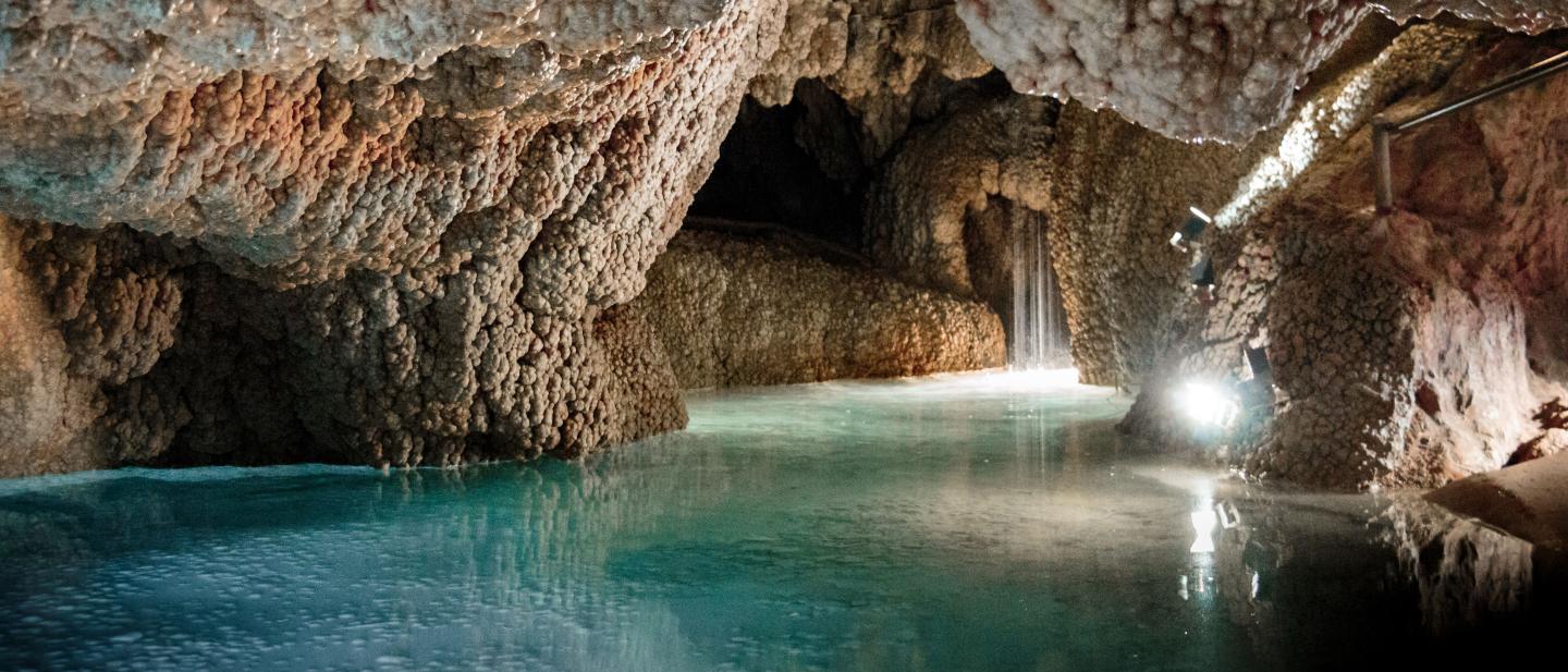 Ein kleiner, hellblauer See in einer Tropfsteinhöhle.