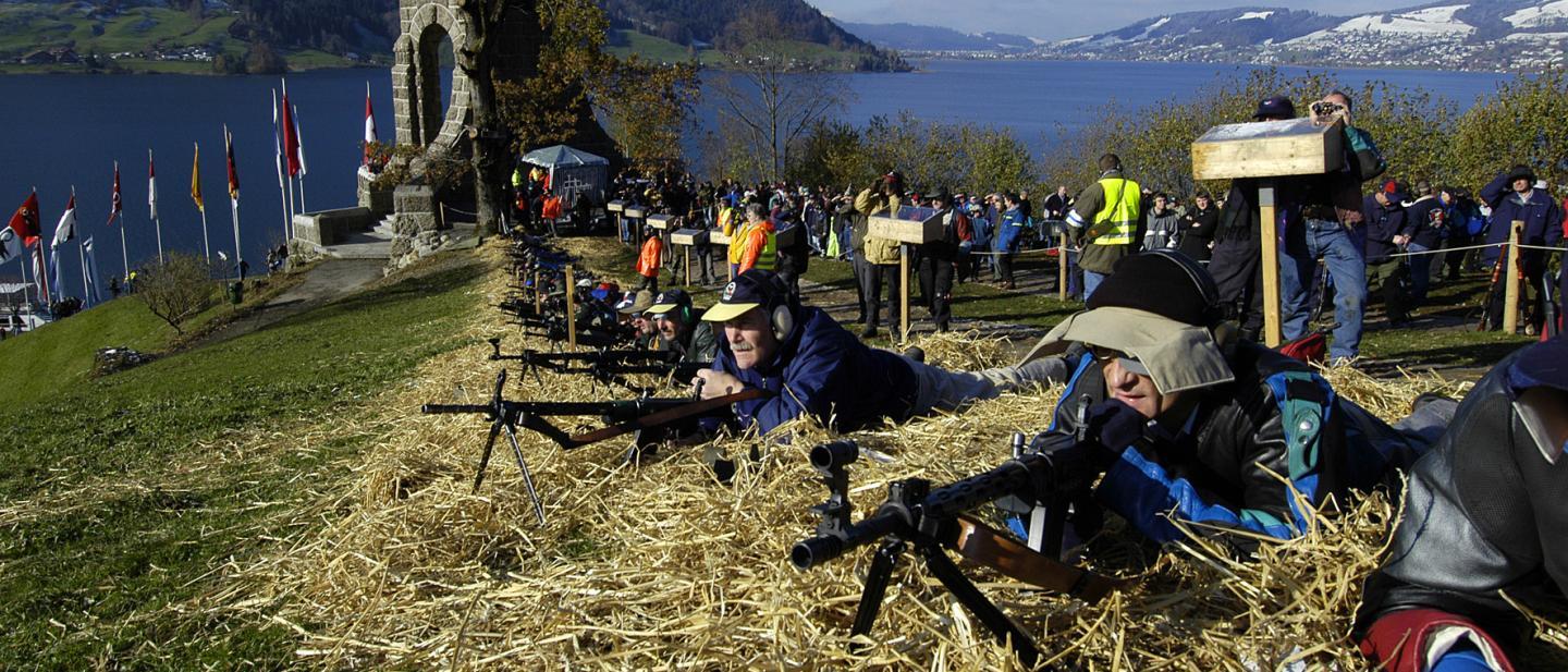Schützen liegen vor dem Morgartendenkmal und schiessen in die Landschaft.