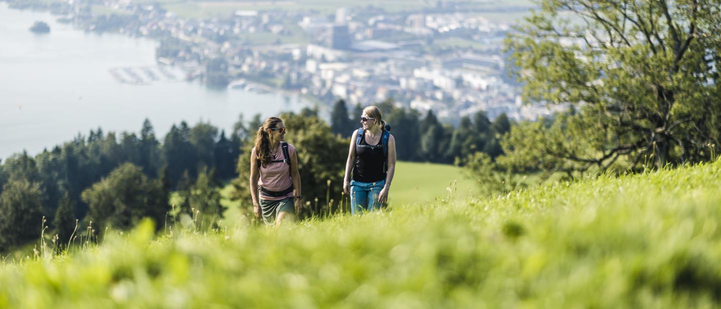 Zwei Frauen wandern auf den Zugerberg. Im Hintergrund ist der See und die Stadt Zug zu sehen.