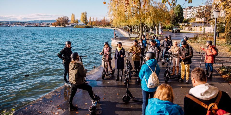Eine Gruppe Menschen steht mit Elektroscootern am Ufer des Zugersees.
