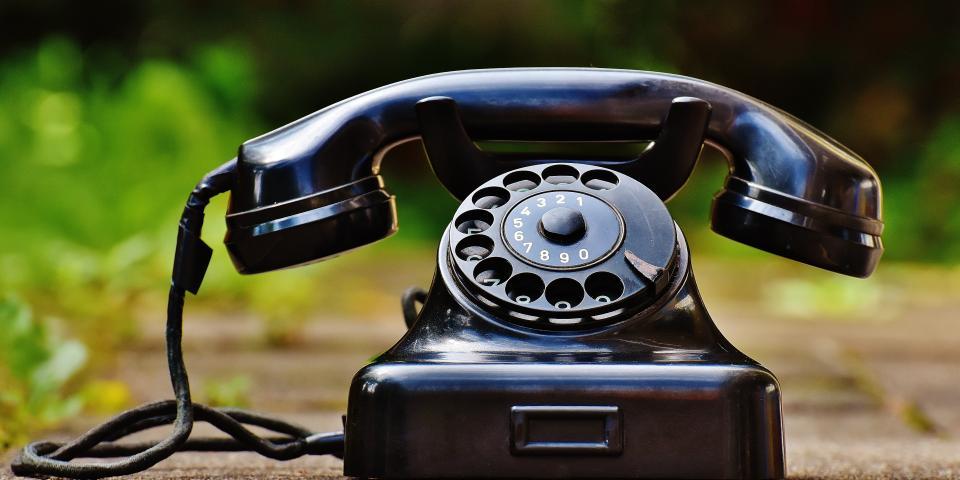 Ein altes, schwarzes Telefon mit Wählscheibe steht vor einem unscharfen, grünen Hintergrund.