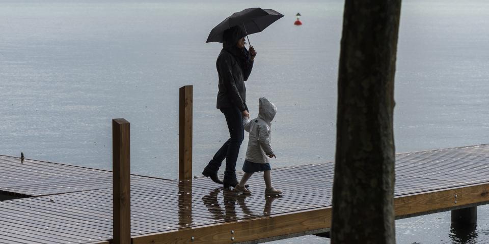 Eine Frau und ein Kind laufen bei Regen über einen Holzsteg am Zugersee.