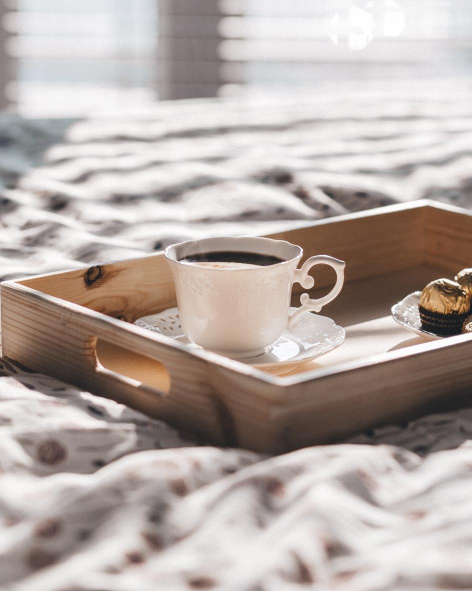 Kaffeetasse mit Schokolade steht auf einem Holztableau auf einem Bett.