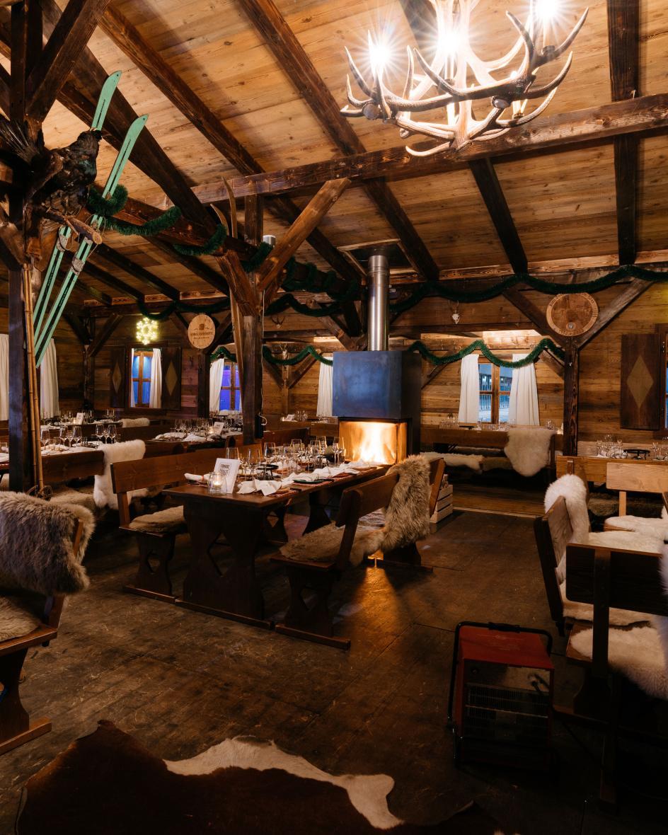 Ein rustikales Restaurant aus Holz mit Fellen auf Stühlen und Hirschgeweih-Lampen.