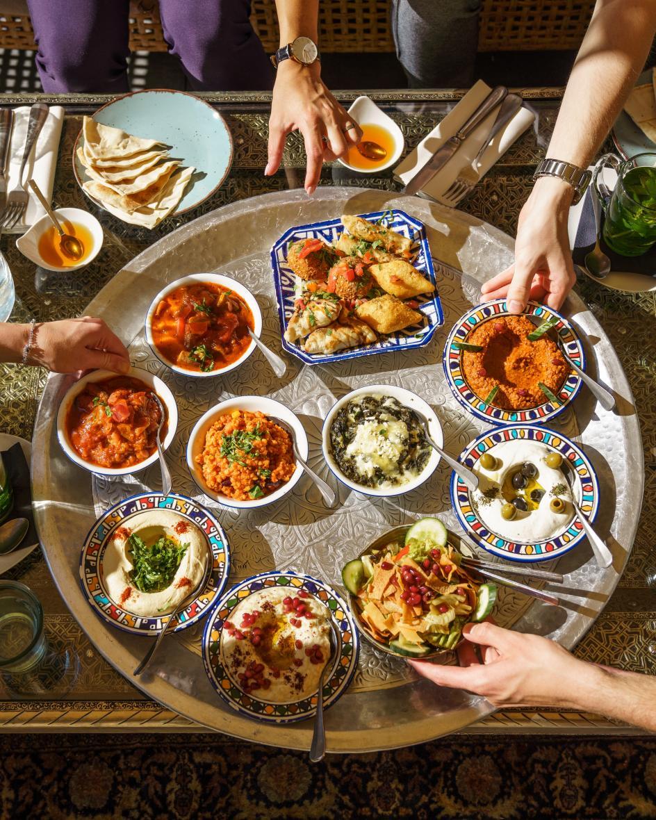 Ein Tisch ist bedeckt mit Mezze Gerichen und vier Hände greifen nach den Speisen.