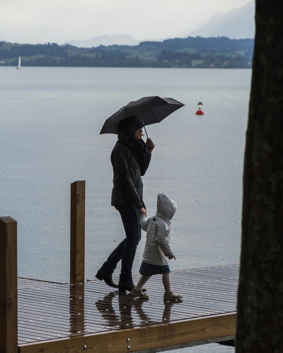 Eine Frau und ein Kind laufen bei Regen über einen Holzsteg am Zugersee.