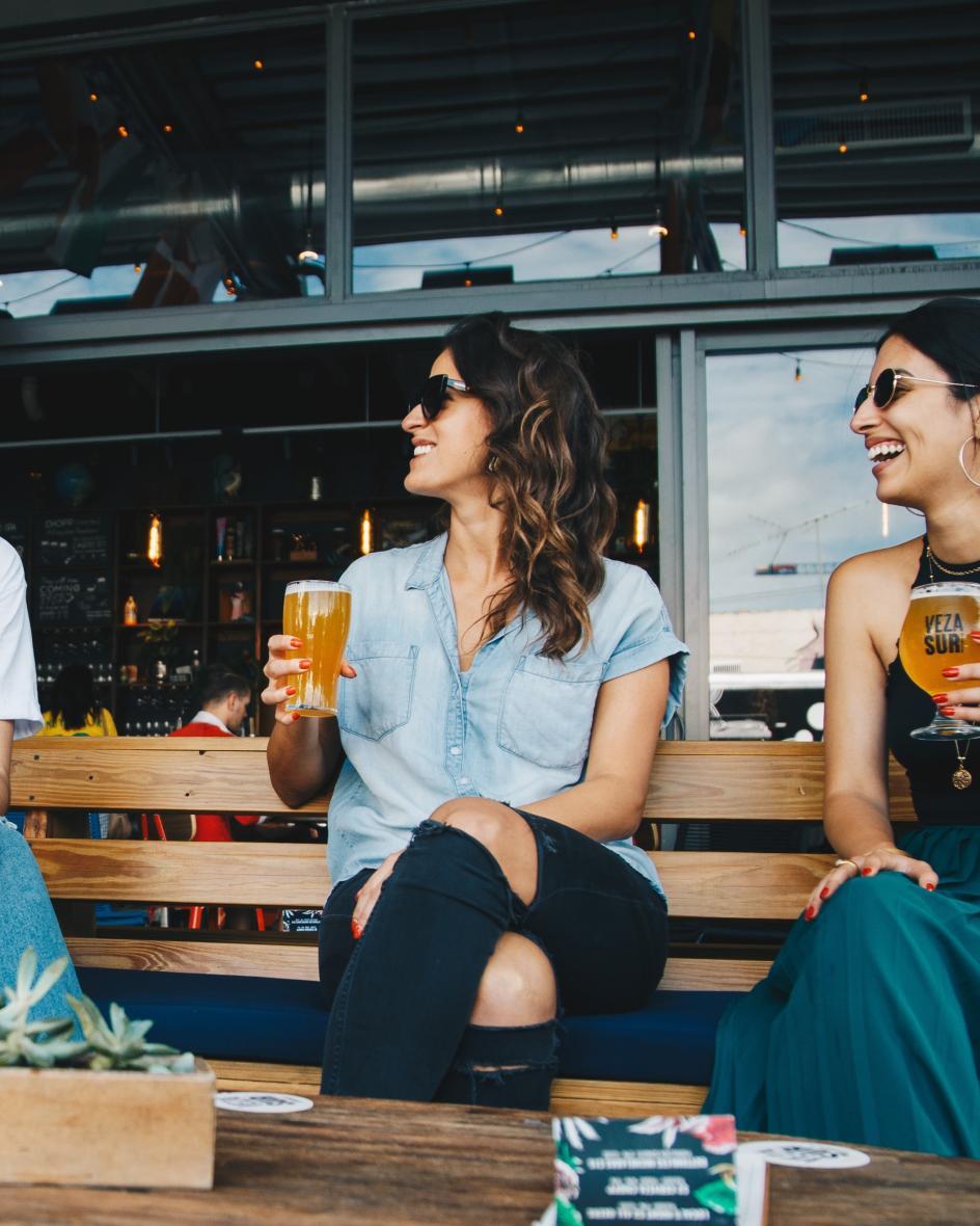 Drei Freundinnen sitzen auf einer Bank und trinken ein Bier.
